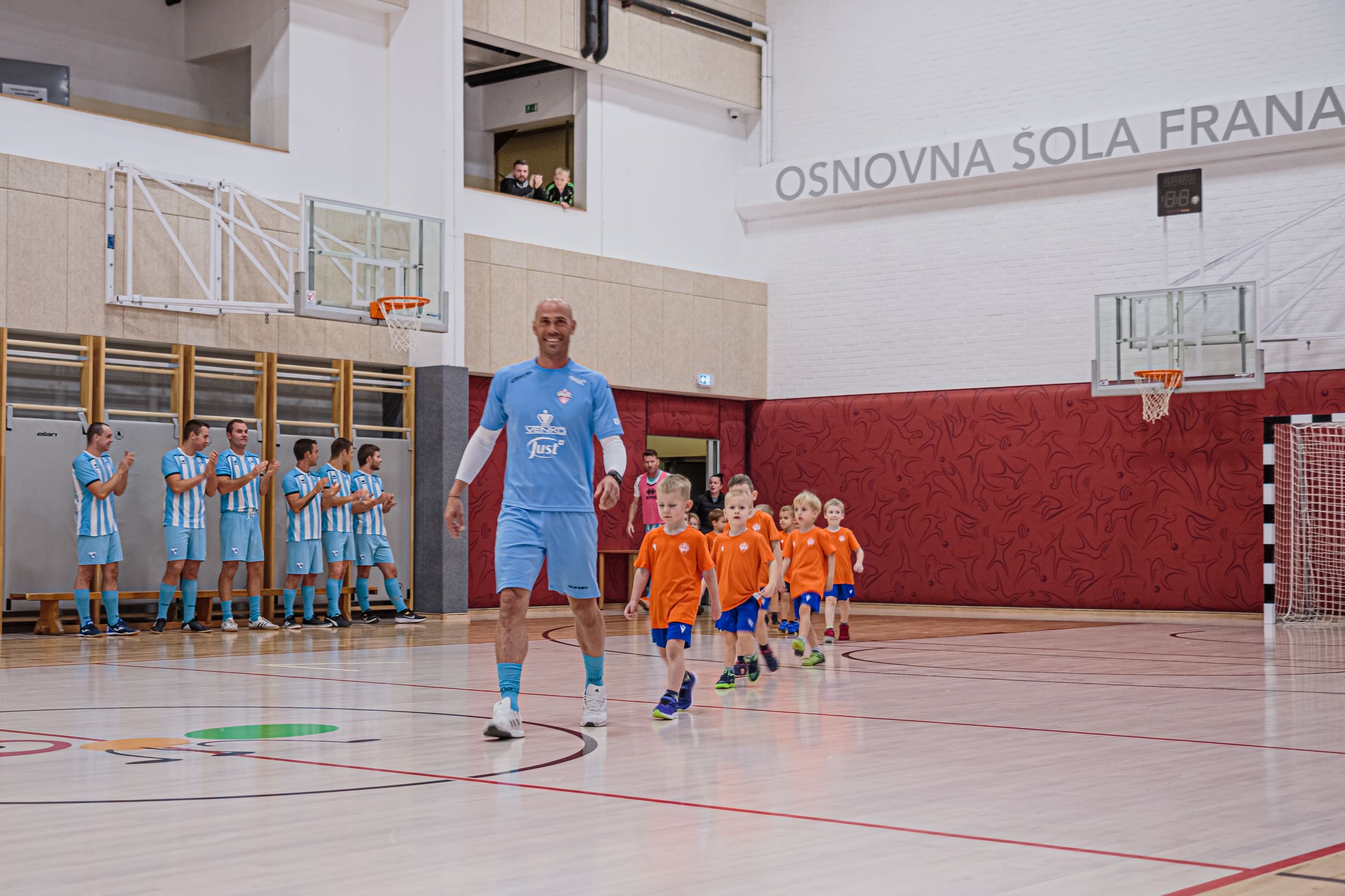 Otroci v oranžno-plavih-dresih na igrišču.