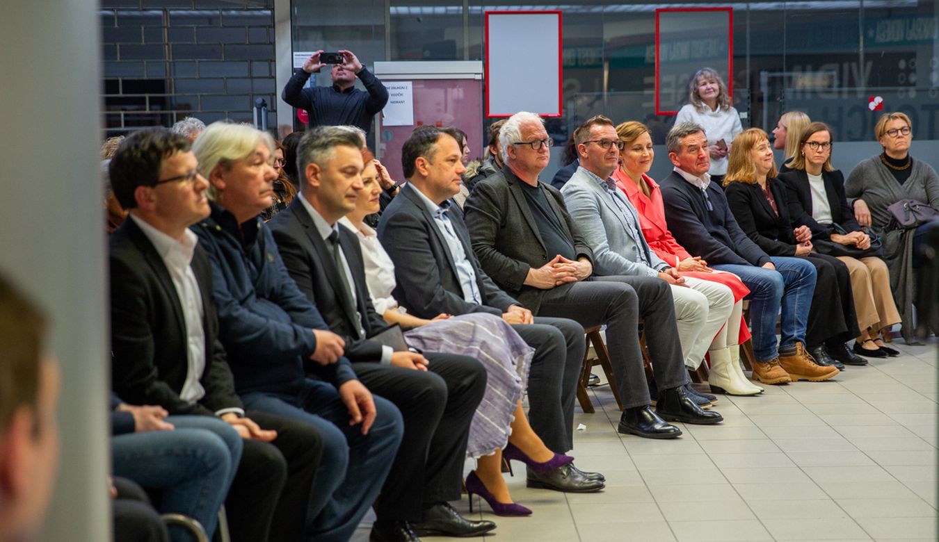 Več oseb sedi v prvi vrsti med uradnim odprtjem. Med sedečimi so tudi župan Mestne občine Nova Gorica Samo Turel, ministrica za kulturo Asta Vrečko in britanska veleposlanica v Sloveniji Victoria Harrison.