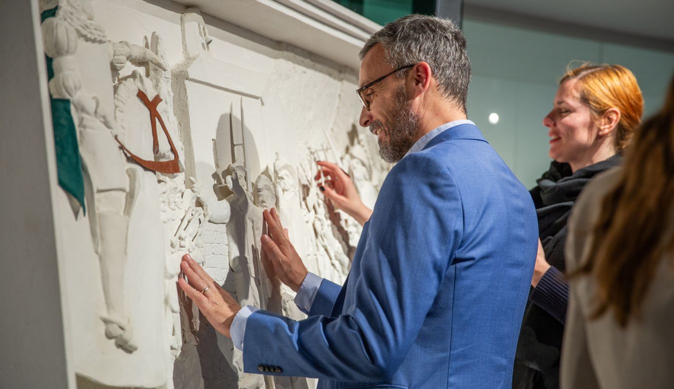 Osebi se dotikata 3D slike v izbočenem profilu, ki je razstavljena v taktilni galeriji. Skulptura predstavlja osebo v srednjeveških oblačilih, ki sedi na konju ter uperja roko proti množici oseb, ki vihtijo vile, kose ipd. 