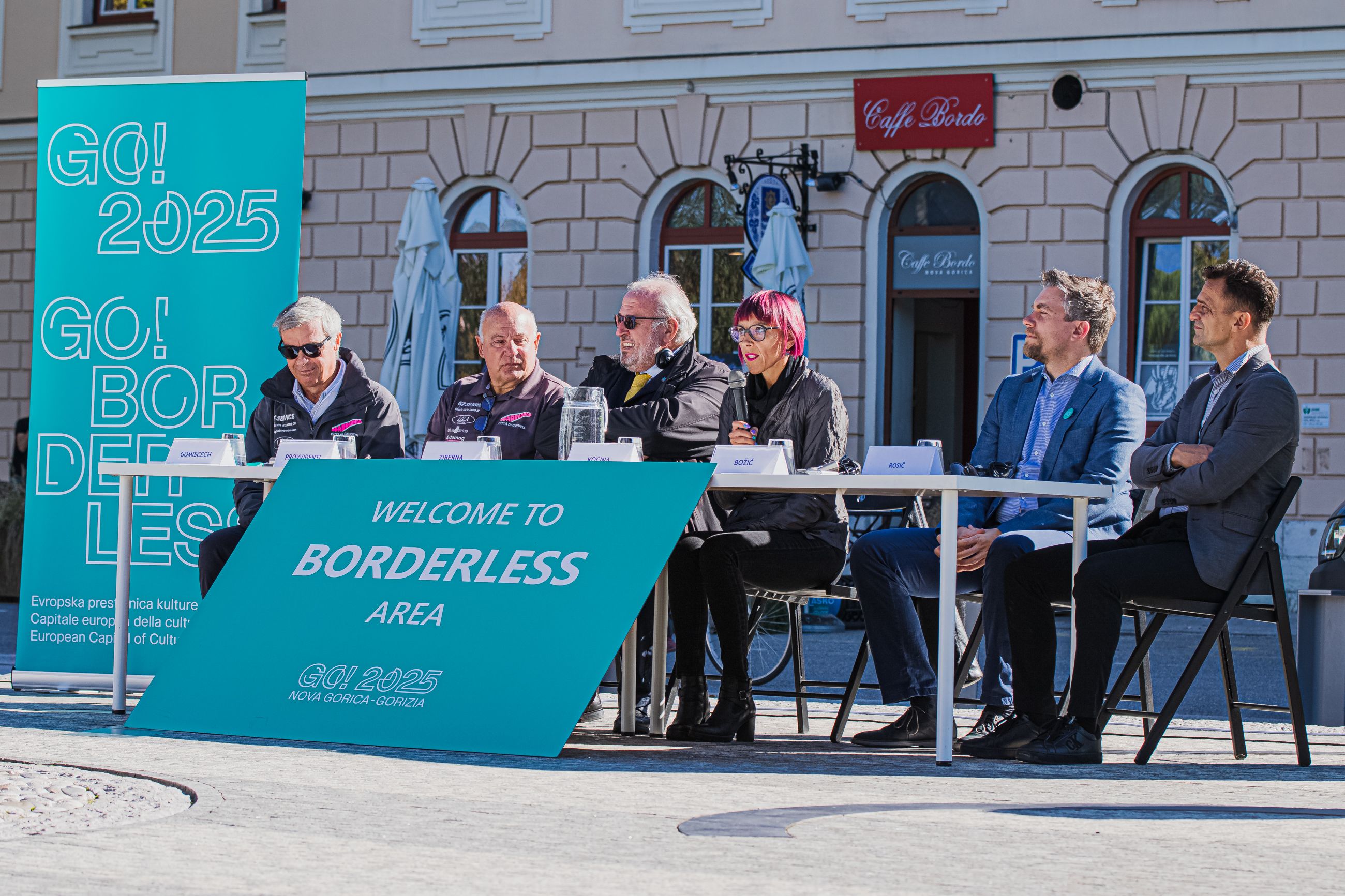 Govorci na novinarski konferenci sedijo pri mizi na Trgu Evrope.
