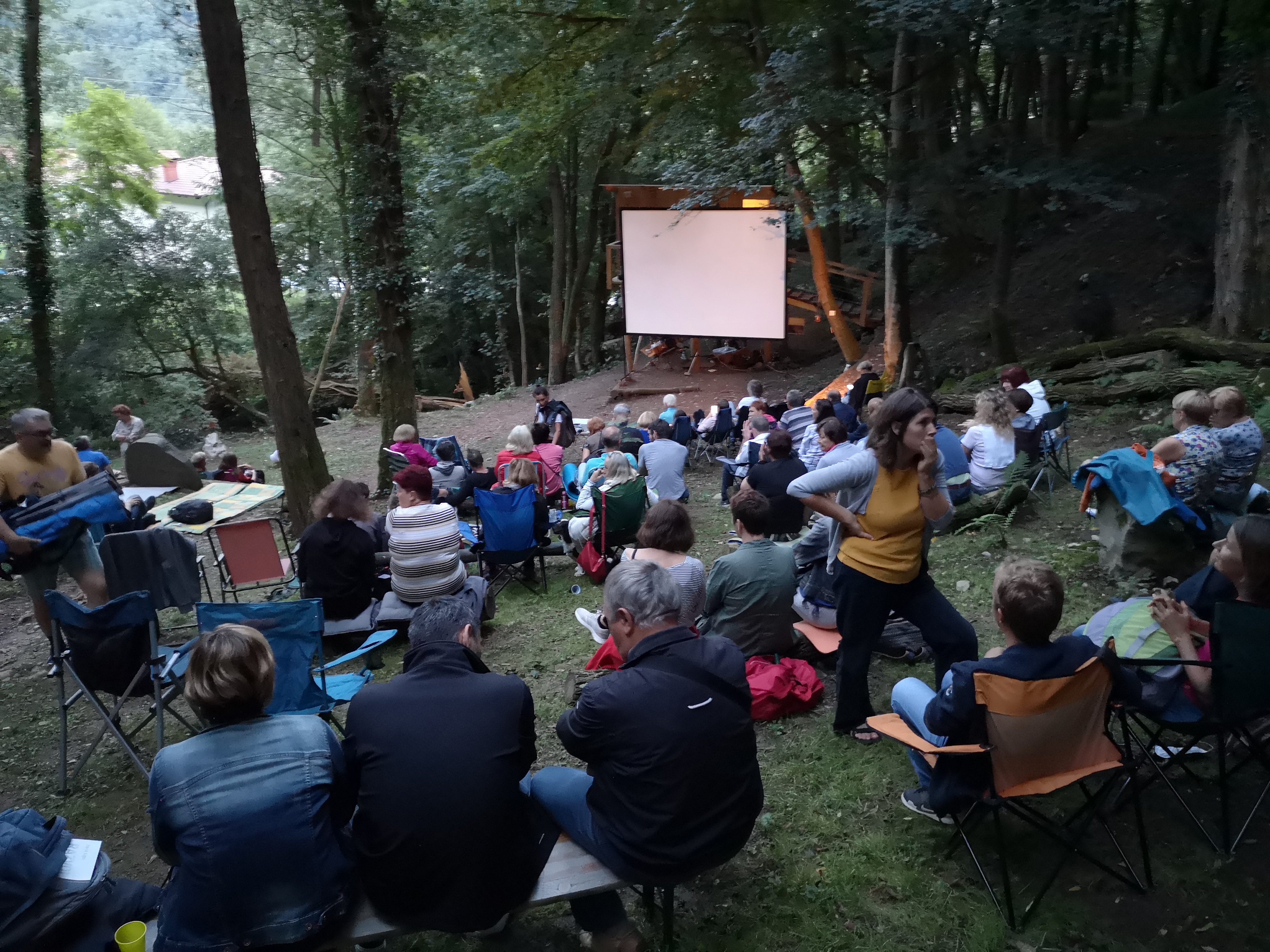 Kino V gozdu, ljudje sedijo v gozdu in gledajo v filmsko platno