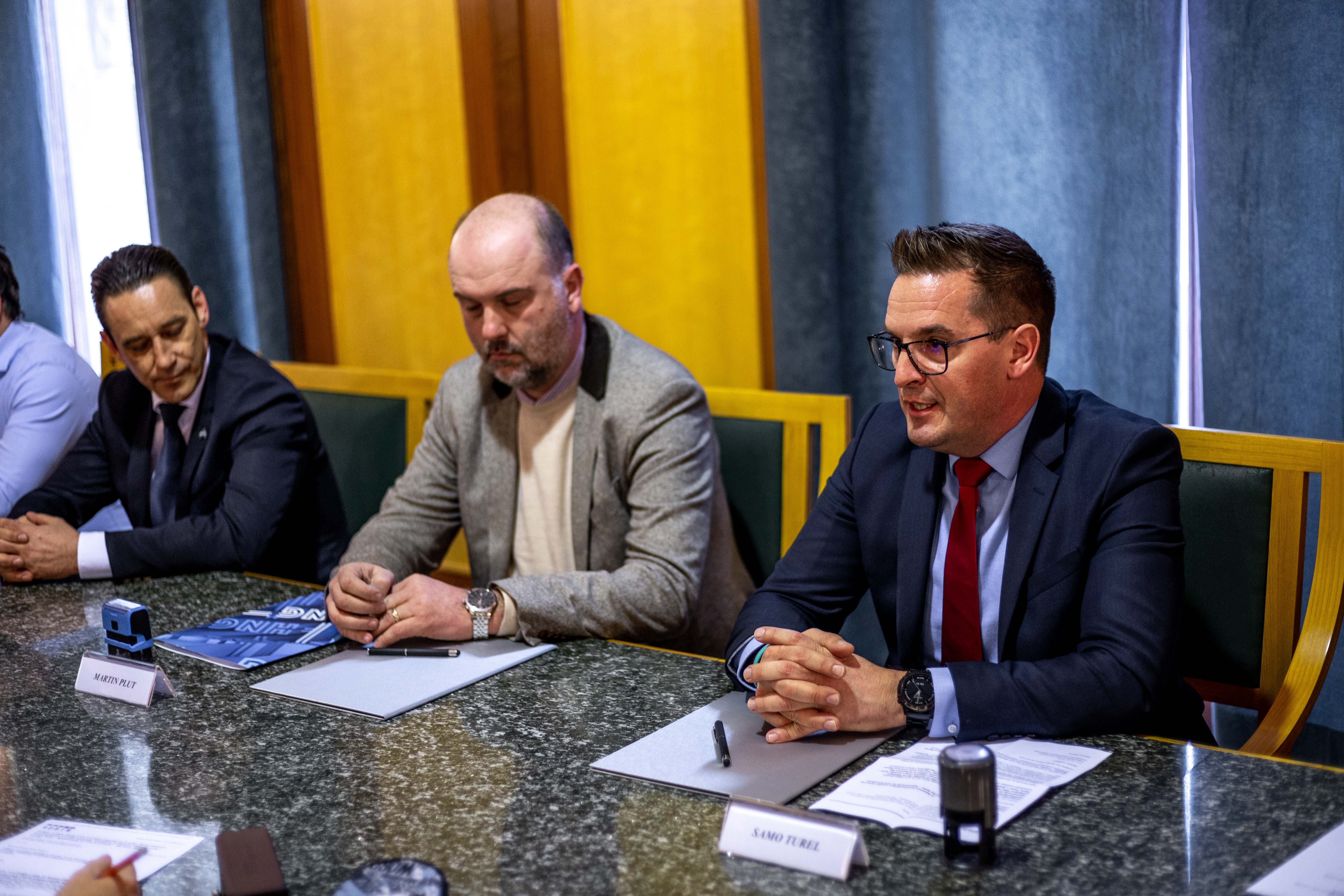 Župan Samo Turel z dvema predstavnikoma podjetja sedi za mizo v zeleni dvorani mestne občine