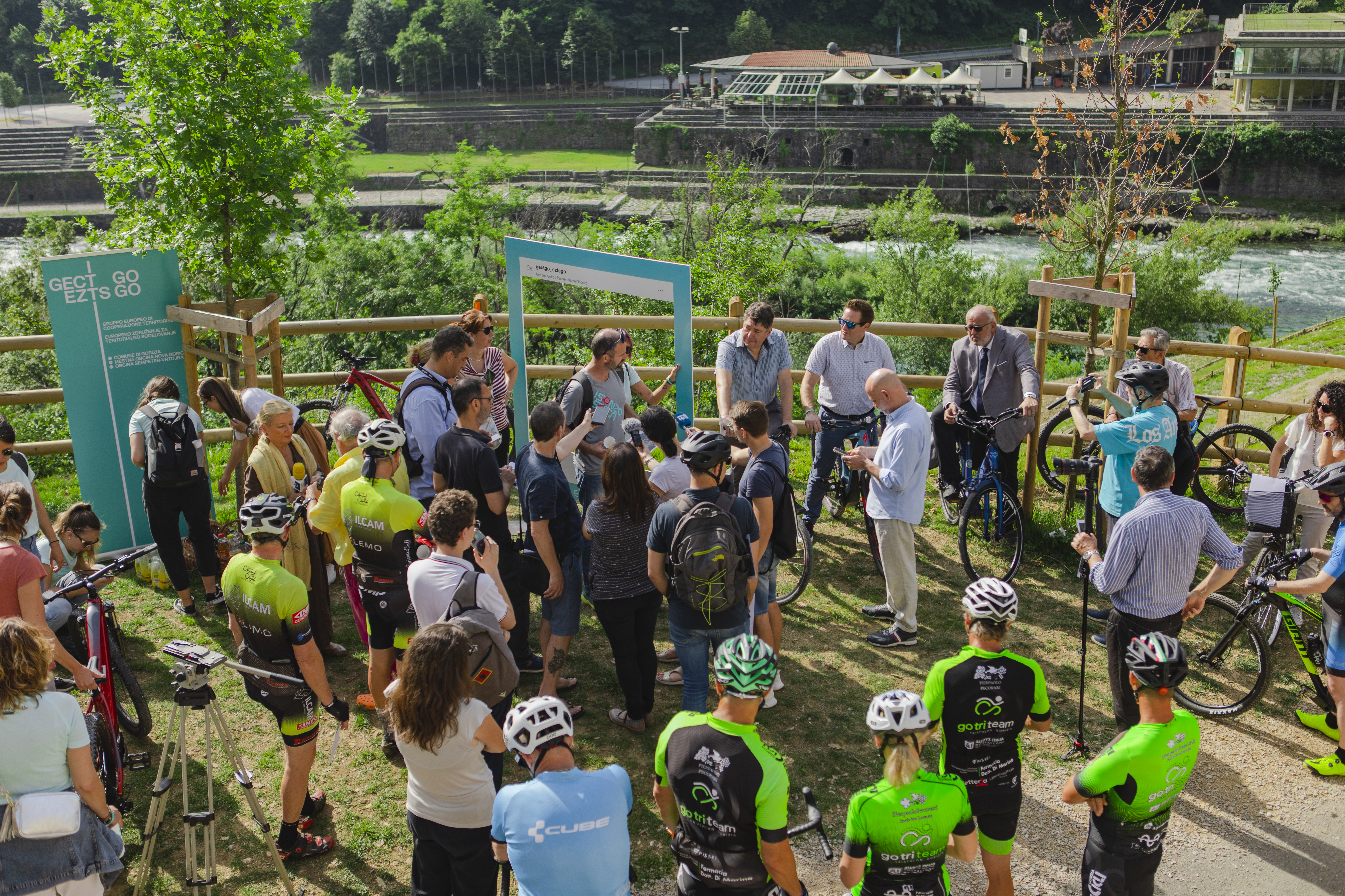 Udeleženci tiskovne konference ter kolesarji stojijo na kolesarski stezi ob reki Soči.