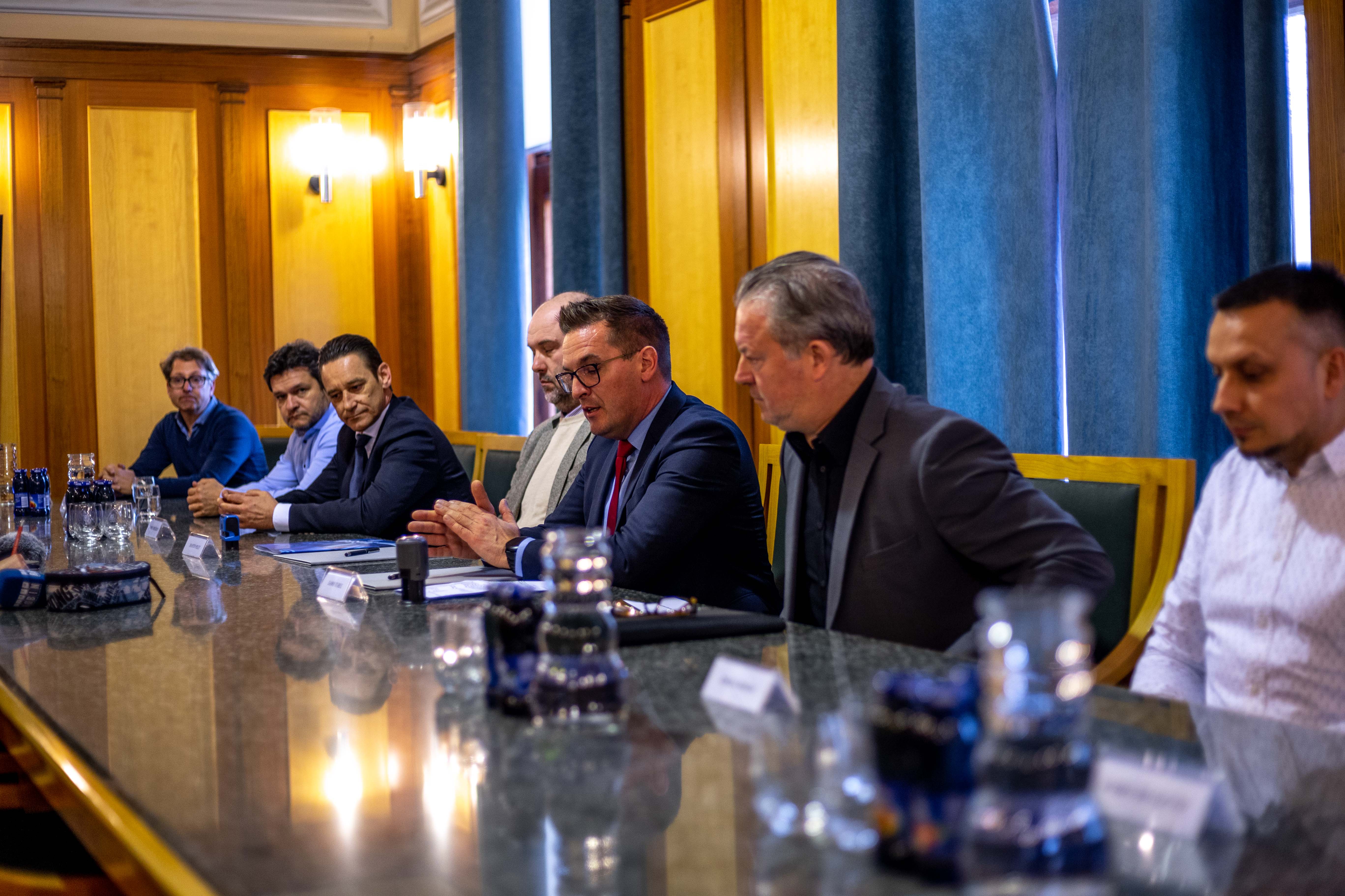 Predstavniki mestne občine in podjetja Hidrotehnika sedijo za mizo v zeleni dvorani mestne občine