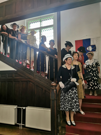 Članice društva aleksandrink stoječe na stopnišču oblečene v starinske obleke